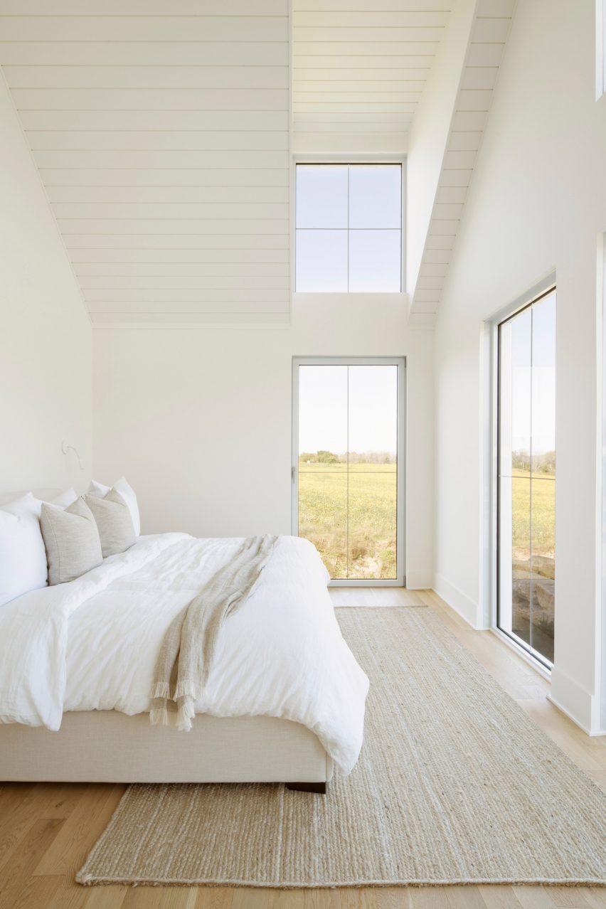 Un dormitorio con paredes blancas, pisos de madera y una cama con ropa de cama blanca