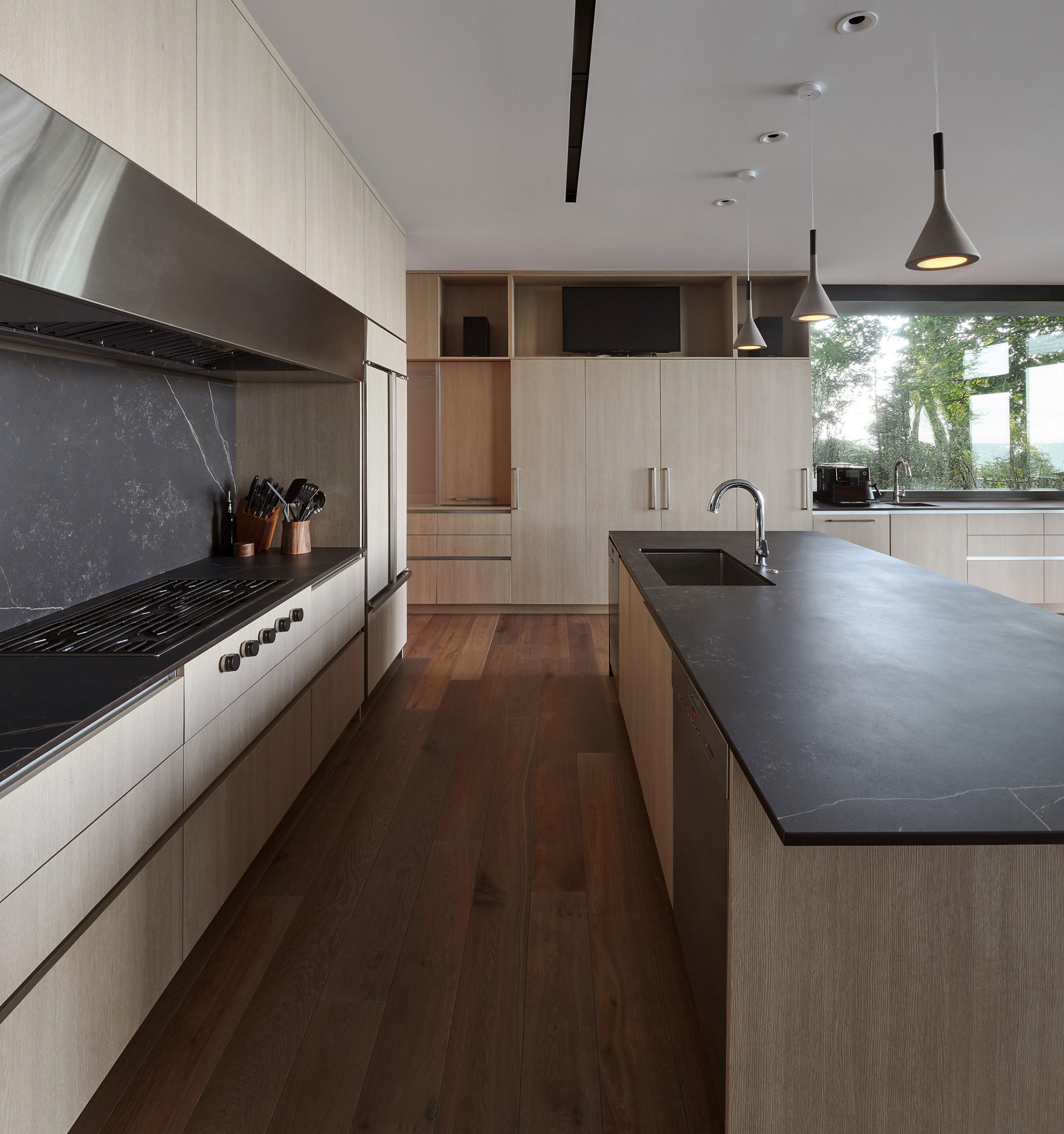 A kitchen with wood flooring, wood kitchen units and a kitchen island with a dark countertop