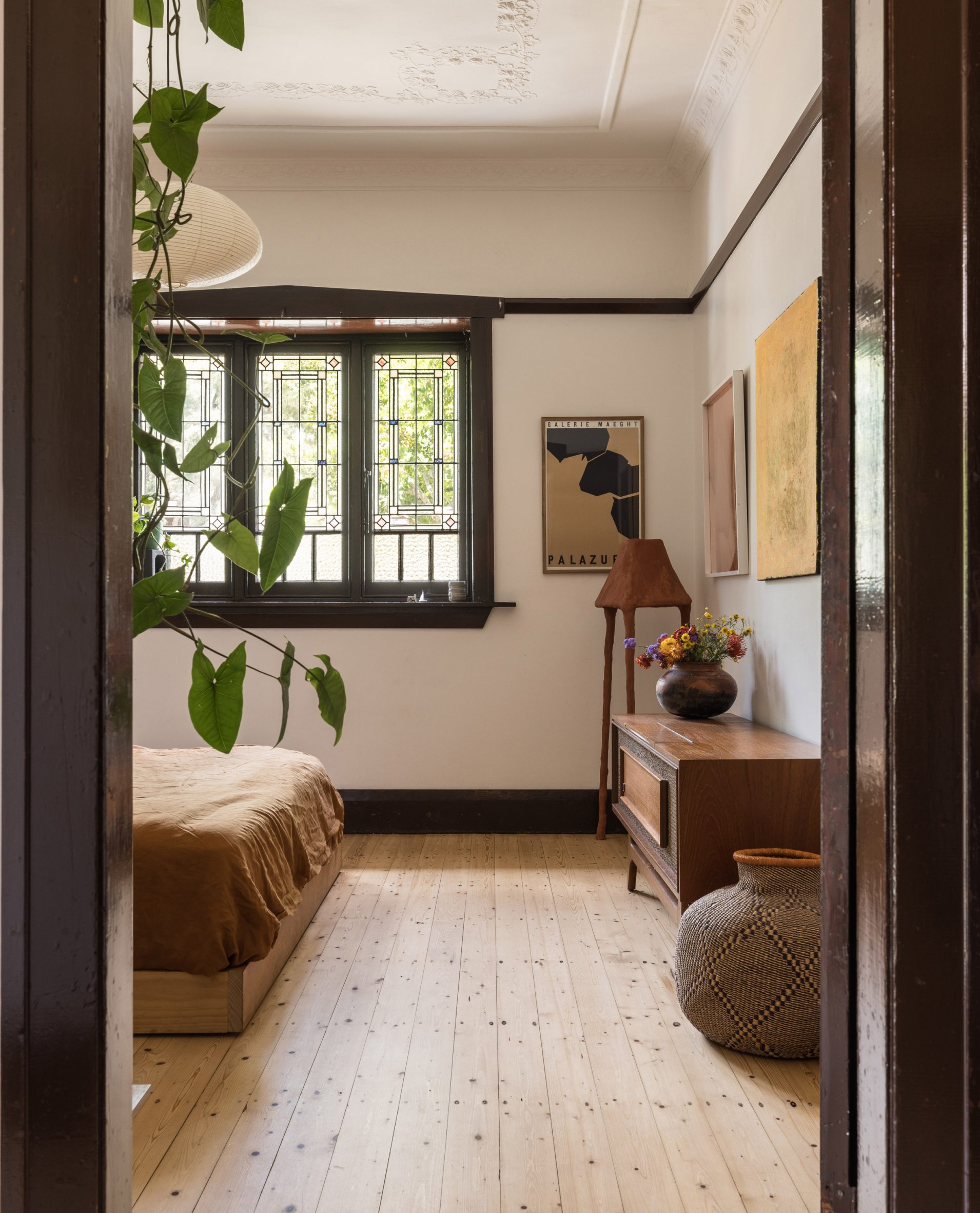 A bedroom with wood floors and dark timber window frames and picture rails
