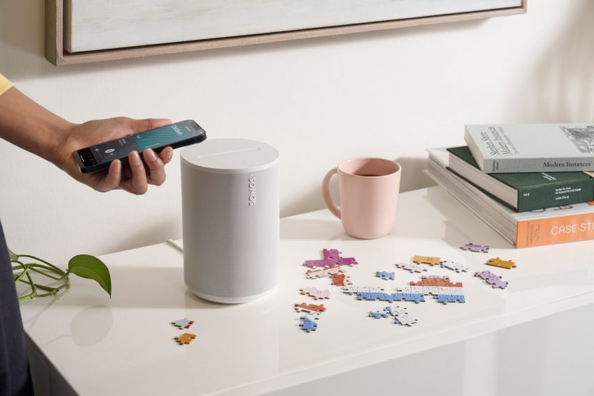 Sonos' Era 100 smart speaker on a sideboard with puzzle pieces and books nearby