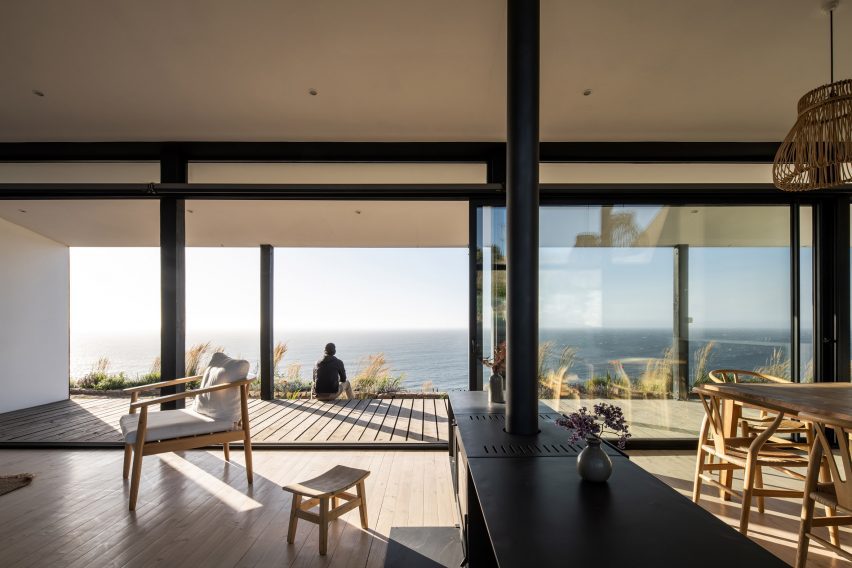 Interior de una casa de planta abierta con grandes puertas corredizas de vidrio que se abren a una terraza con vista al mar