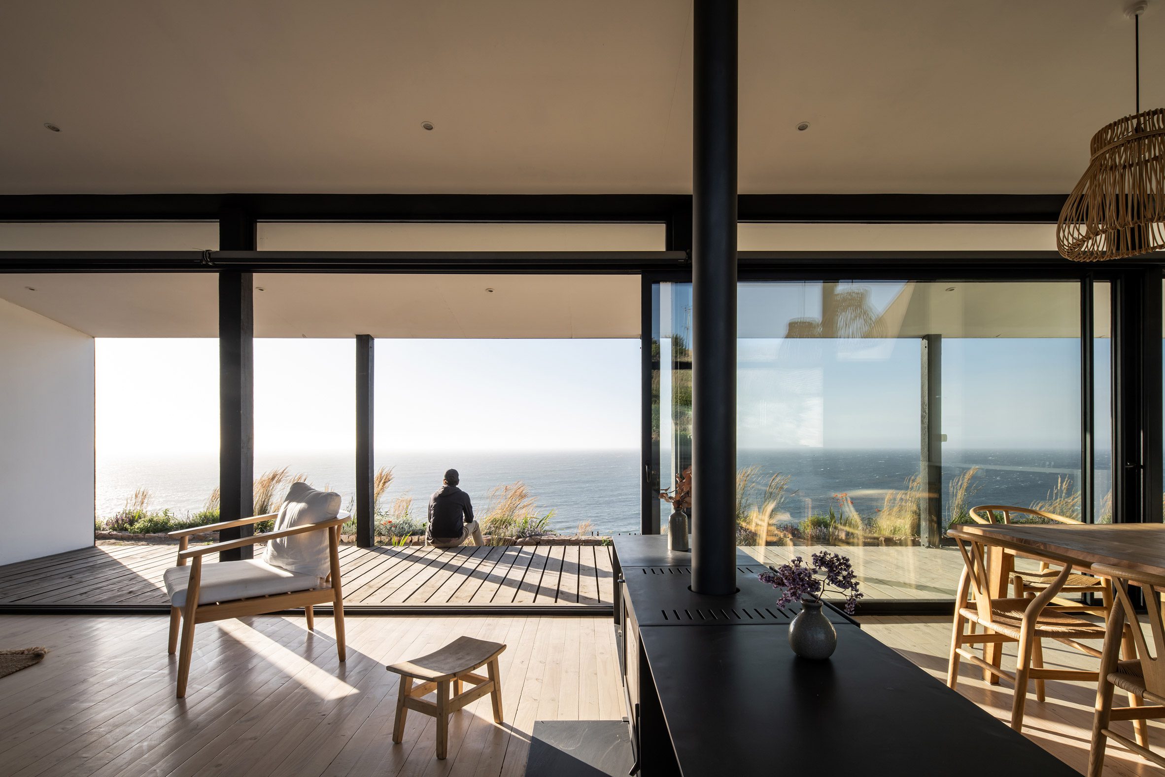 Interior of an open-plan home with large glass sliding doors opening to decking overlooking the sea