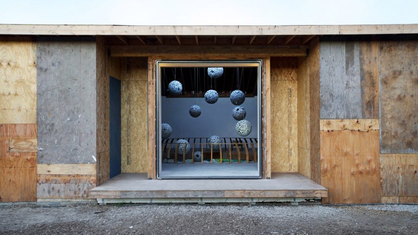 Plywood building with a square opening revealing orbs hanging from the ceiling