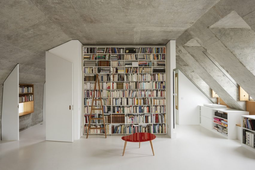 Loft space with concrete ceilings and a floor-to-ceiling bookshelf and a red coffee table