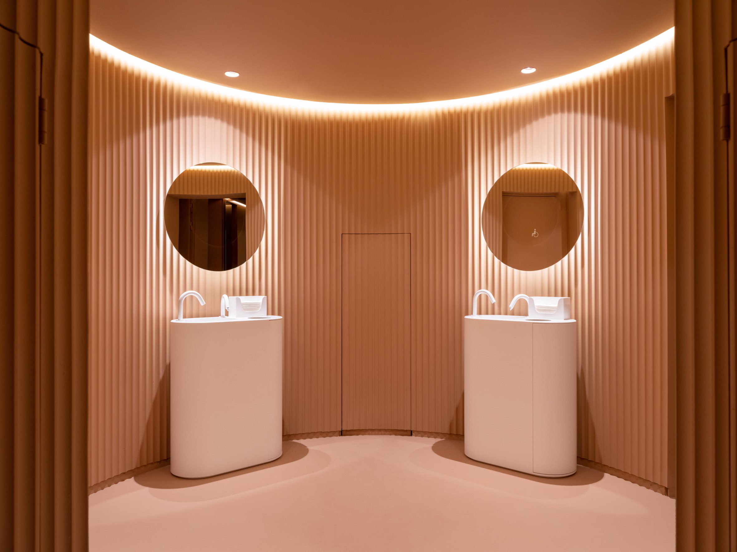 Peach public bathroom interior with two freestanding sinks and circular mirrors