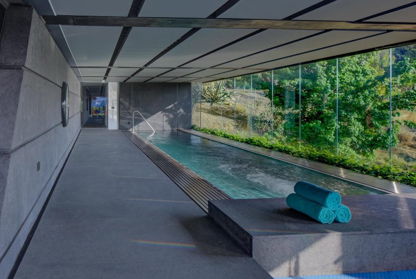 Indoor swimming pool with dark grey flooring and glazed wall overlooking a garden