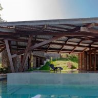 A terrace with a swimming pool with an angular metal roof supported by a wooden structure
