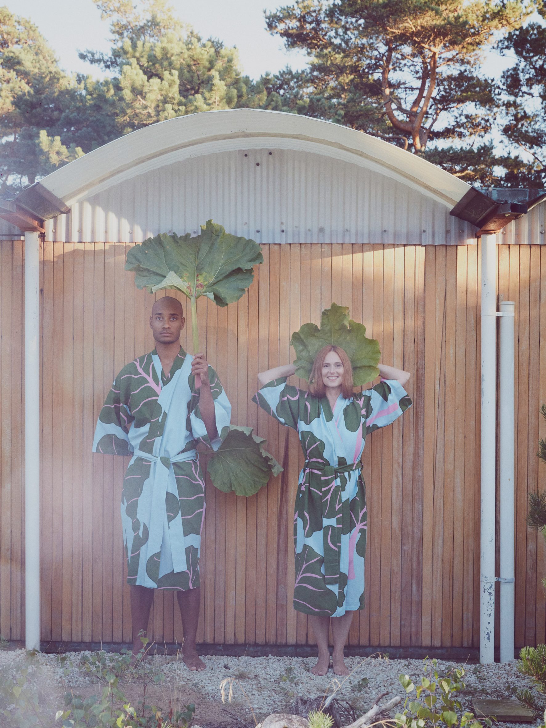Two people wearing blue and green printed bathrobes holding up large leaves
