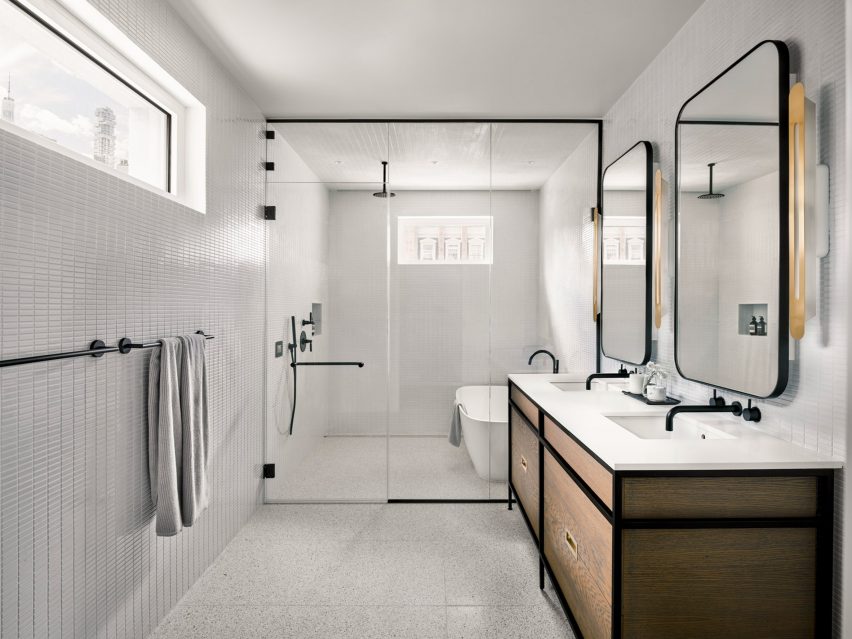 فضای داخلی یک حمام سفید با یک اتاق نمناک و واحدهای روشویی چوبی