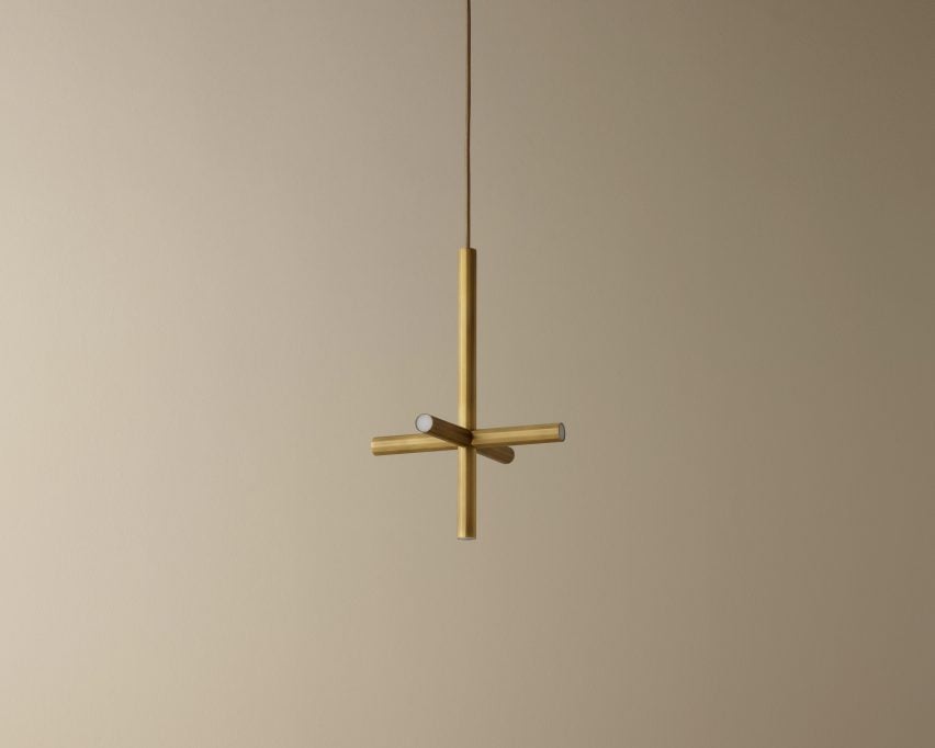Bronze coloured, cross shaped pendant lamp hanging in front of beige wall