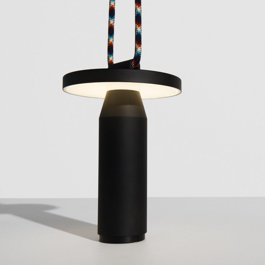 Black lamp with rainbow coloured cord on white table in front of white wall