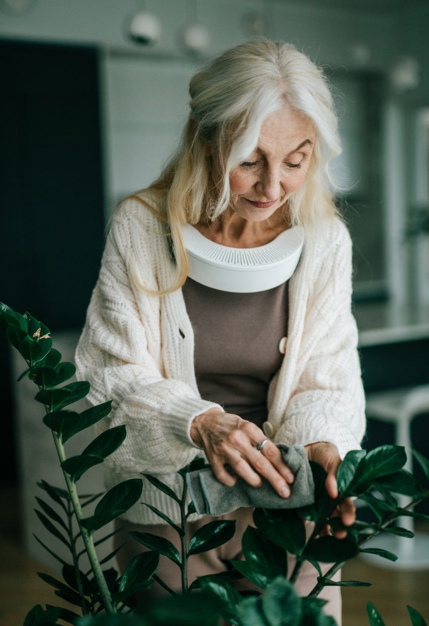 Photo of a woman tending to houseplants while wearing a white personal air purifier around her neck