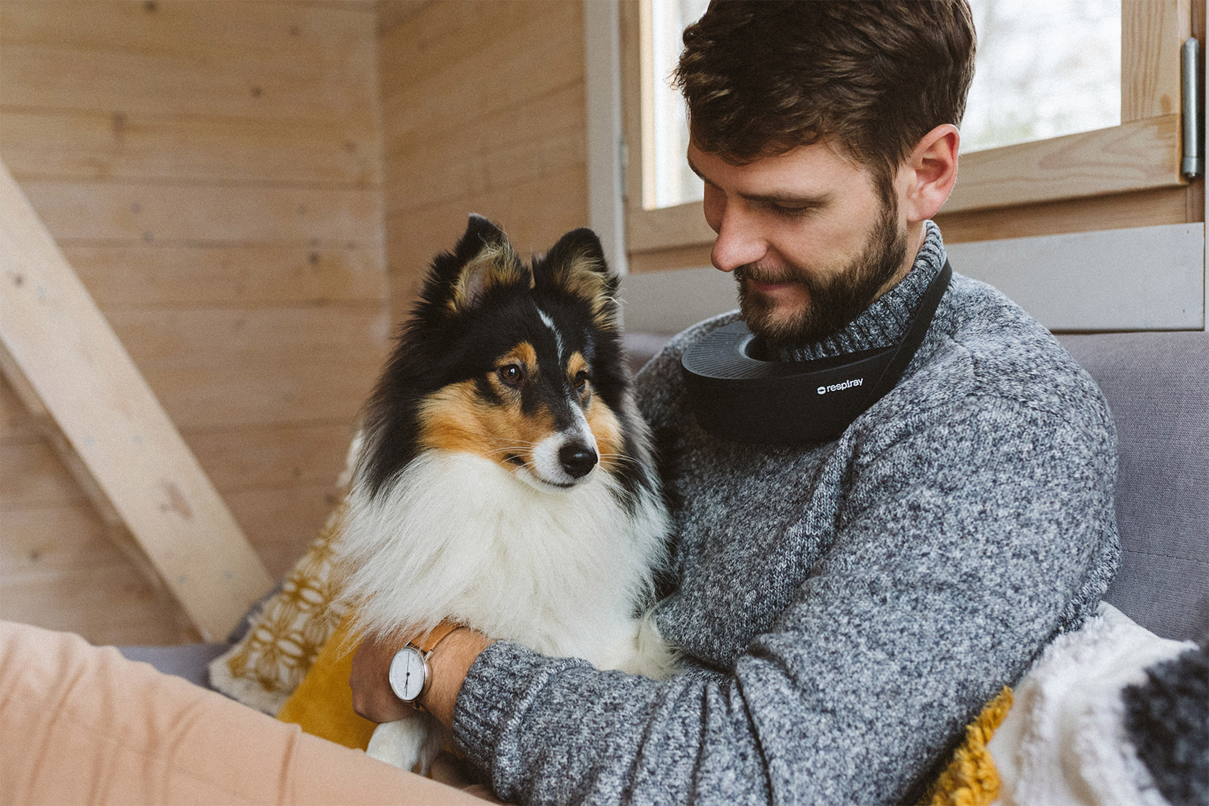 Photo of a man wearing a Respiray device around his neck and hugging a dog