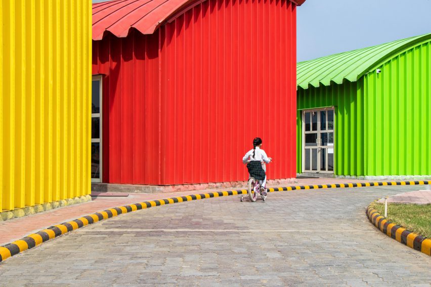 Cobertizos de acero amarillos, rojos y verdes con un niño en bicicleta al frente