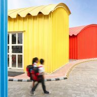 School children walking beside blue, yellow, red and green steel buildings