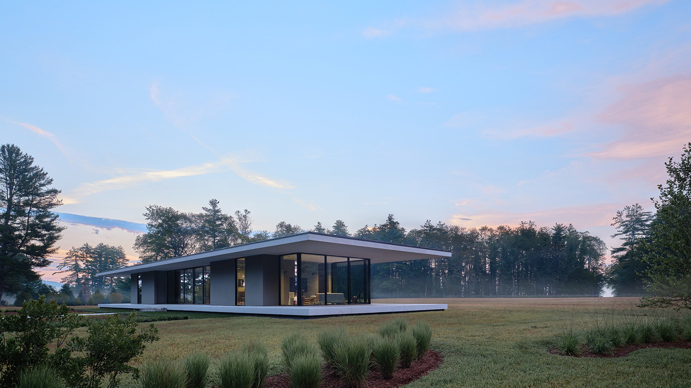 Replanted natural grasses surrounding bungalow-style glass house with large overhangs by Specht Architects