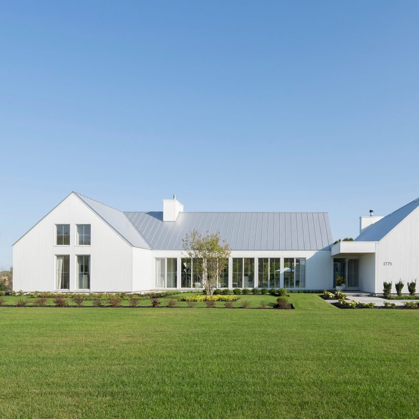 A white U-shaped house with a pitched roof on a green lawn