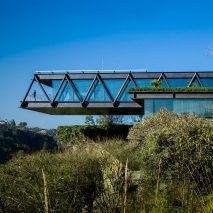 One-storey house with a ddark metal structure cantilevering over bushes