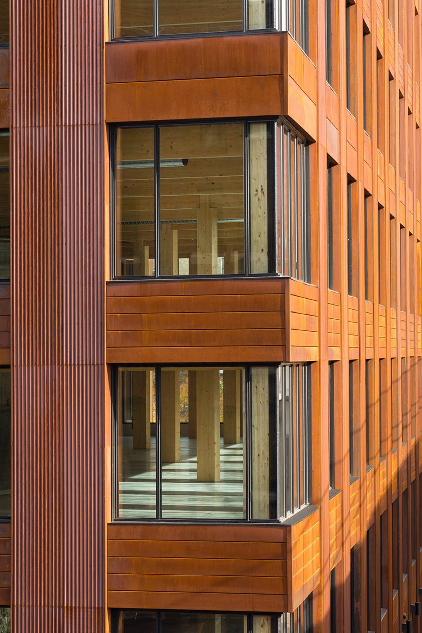 The corner of a weathered-steel-clad building with corner windows looking into an interior with a mass-timber structure