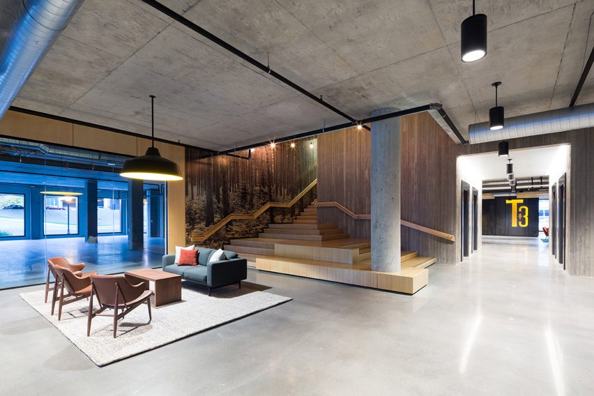 Interior of an office lounge space with concrete floor and ceiling and a wooden staircase
