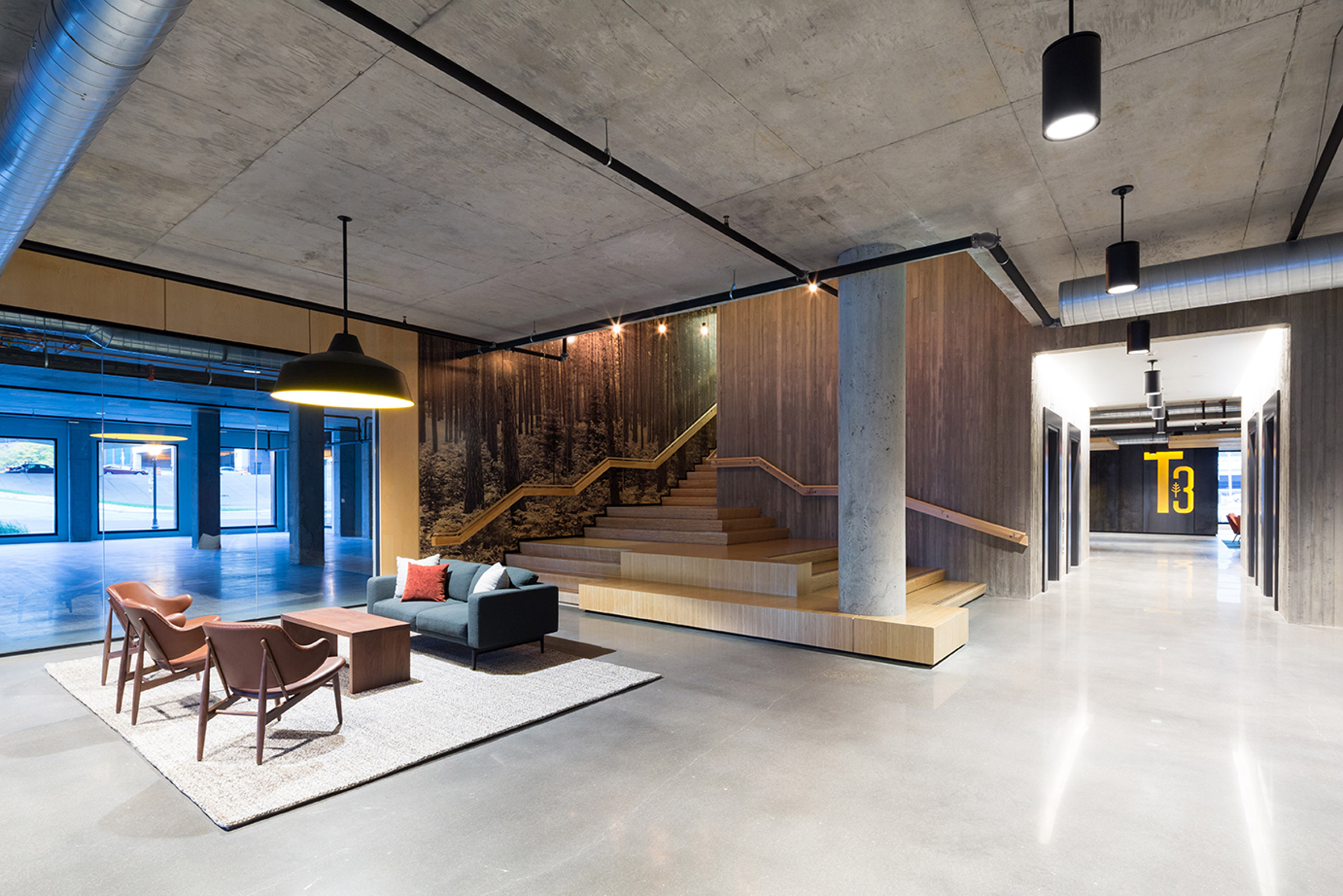 Interior of an office lounge space with concrete floors and ceiling and a wooden staircase