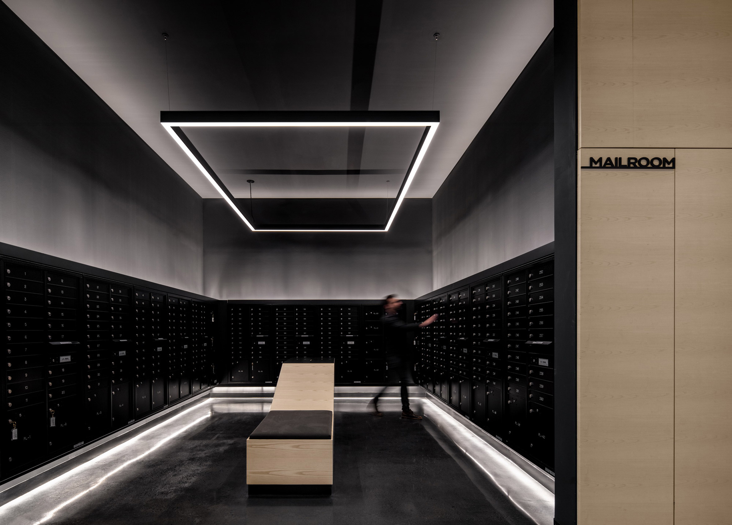 Black and silver mailroom within mixed-use building by Handel Architects with rectilinear LED lighting overhead