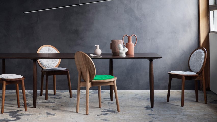 Four wooden chairs by Ca'lyah at a dining table in a dark concrete room