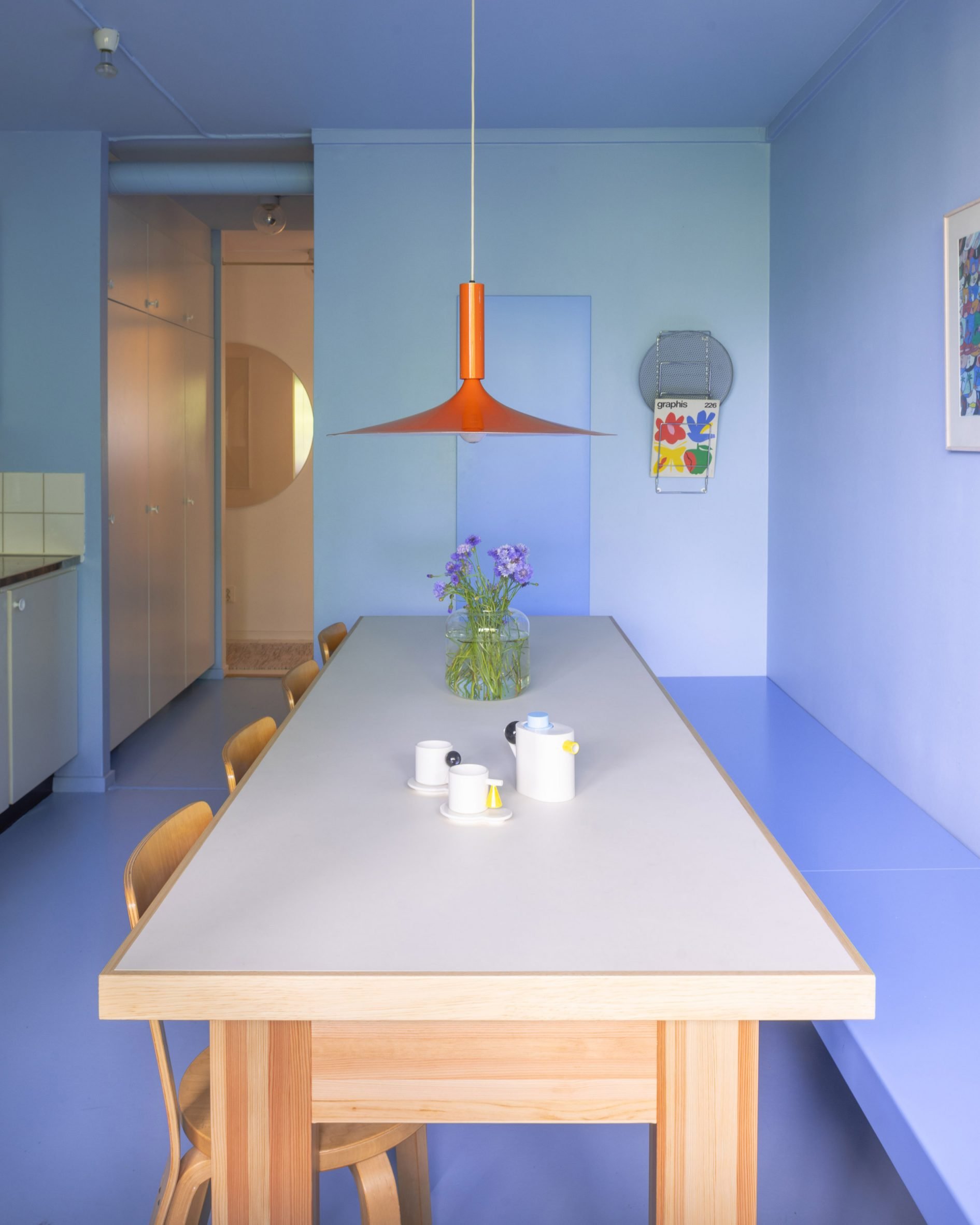 All-lilac kitchen with geometric seating and a bright orange pendant lamp above the dining table
