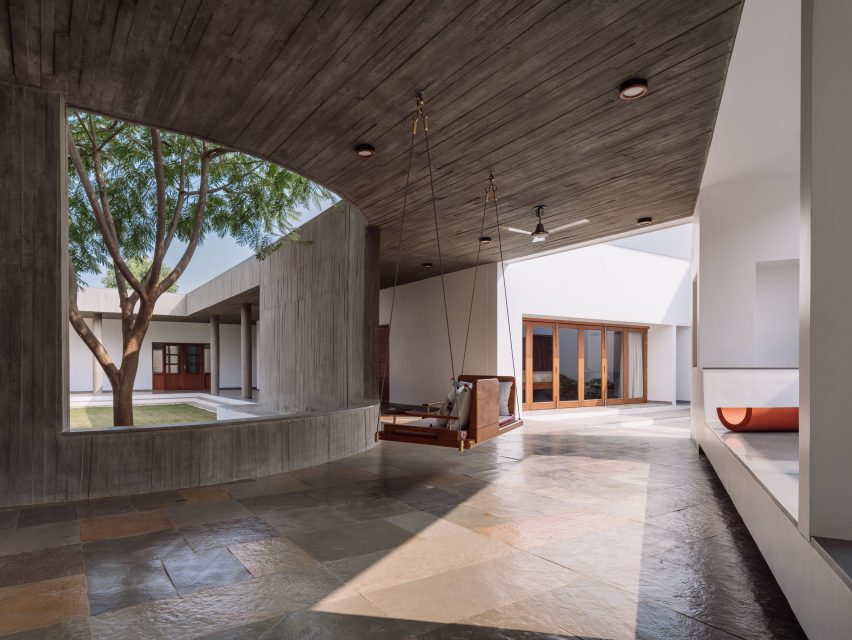 Covered concrete walkway with a swing seat in front of an opening the the wall that overlooks a courtyard