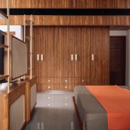 A bedroom with wood-panelled walls, concrete floors and a red throw over the bed