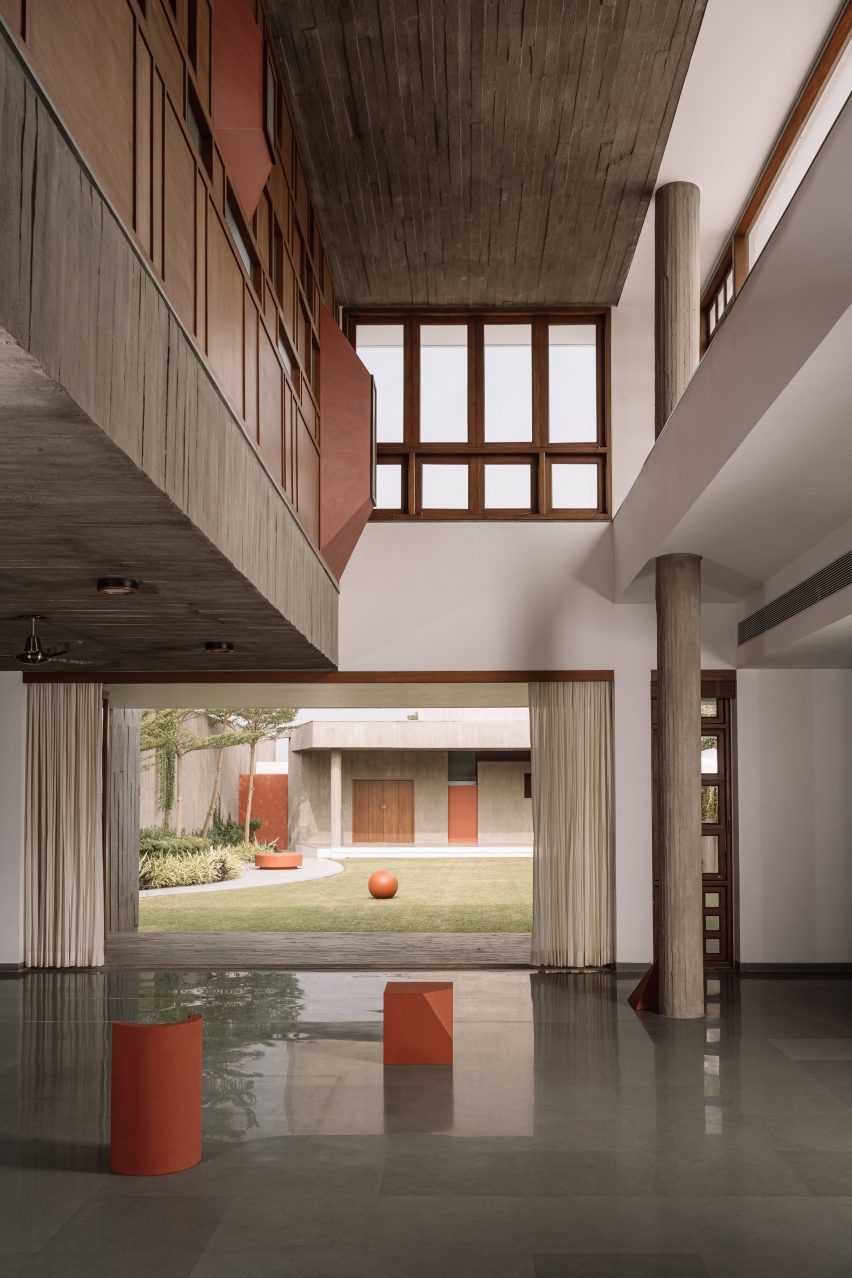 Double-height living space with concrete walls, wooden-framed windows and and opening leading to a courtyard lawn