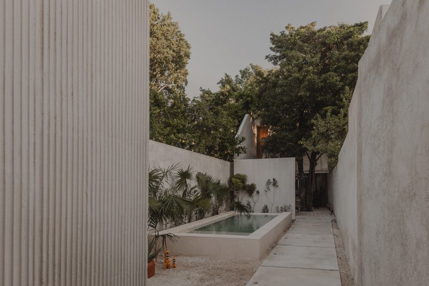 Concrete courtyard with a small swimming pool, concrete perimeter walls and lush green trees