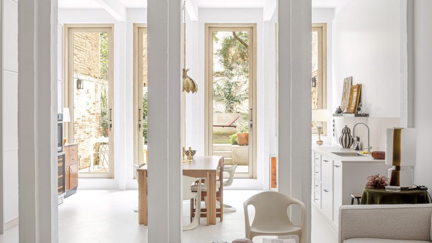 Interior of a white Barcelona apartment with square columns and glass doors leading to a patio