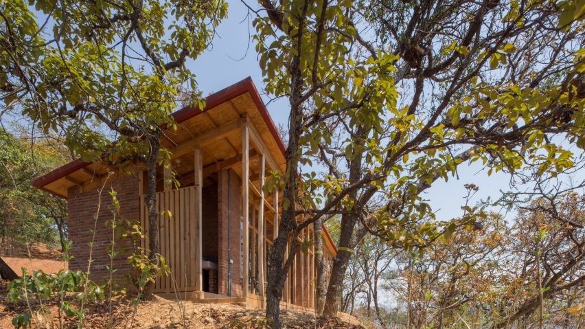 Wooden one-storey shed-like home on a sandy hill in Mexico with trees.