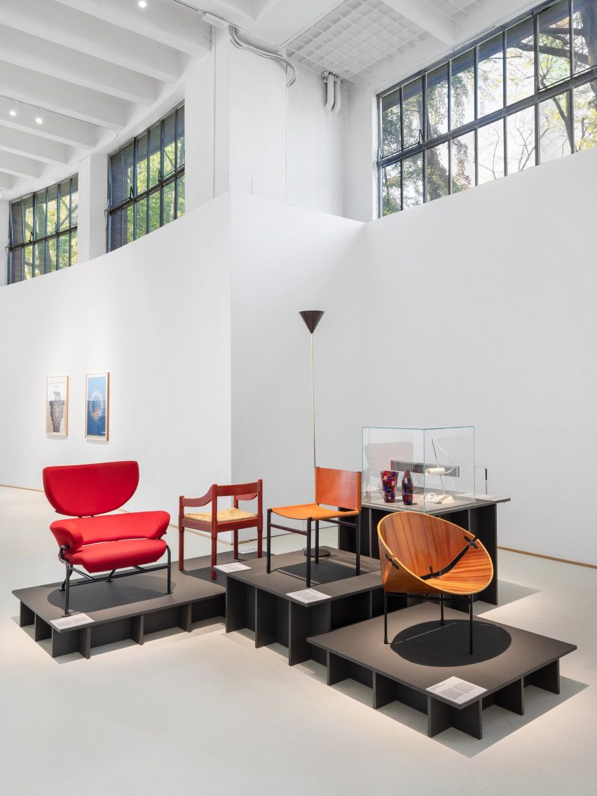 Photo of the Museo del Design Italiano permanent exhibition showing chairs arranged on plinths of different heights and posters framed on the wall in the background