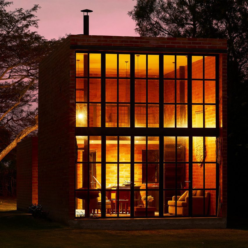 Exterior of a brick micro home with double-height window facade lit up at night