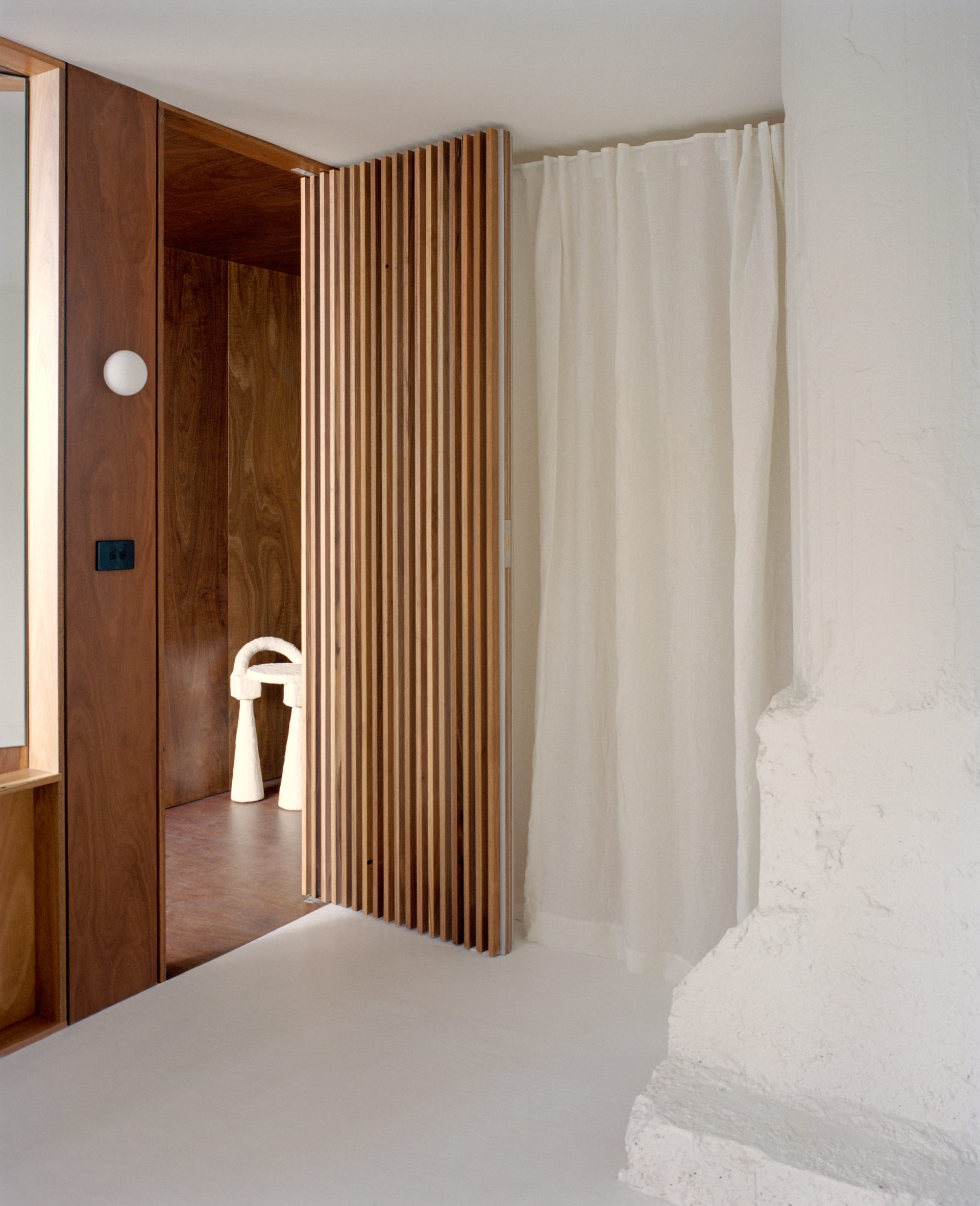 Gridded timber door next to translucent curtains that cordon off a bedroom 