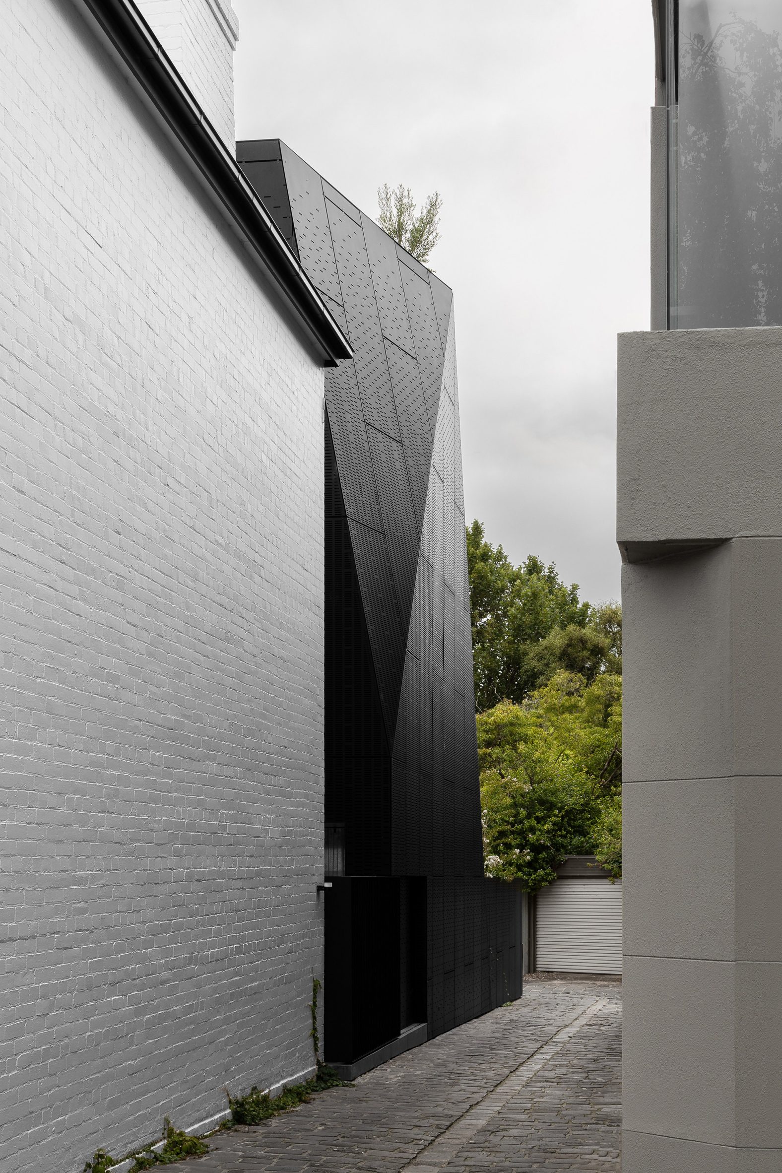 Faceted black extension to white-brick house