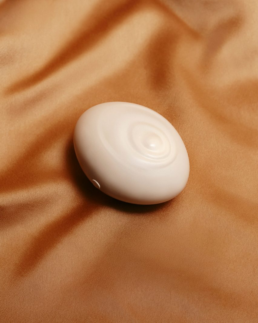 Photograph of a white spheroid massager with a light rippling design on the front, sitting on a rumpled rust-coloured silk sheet