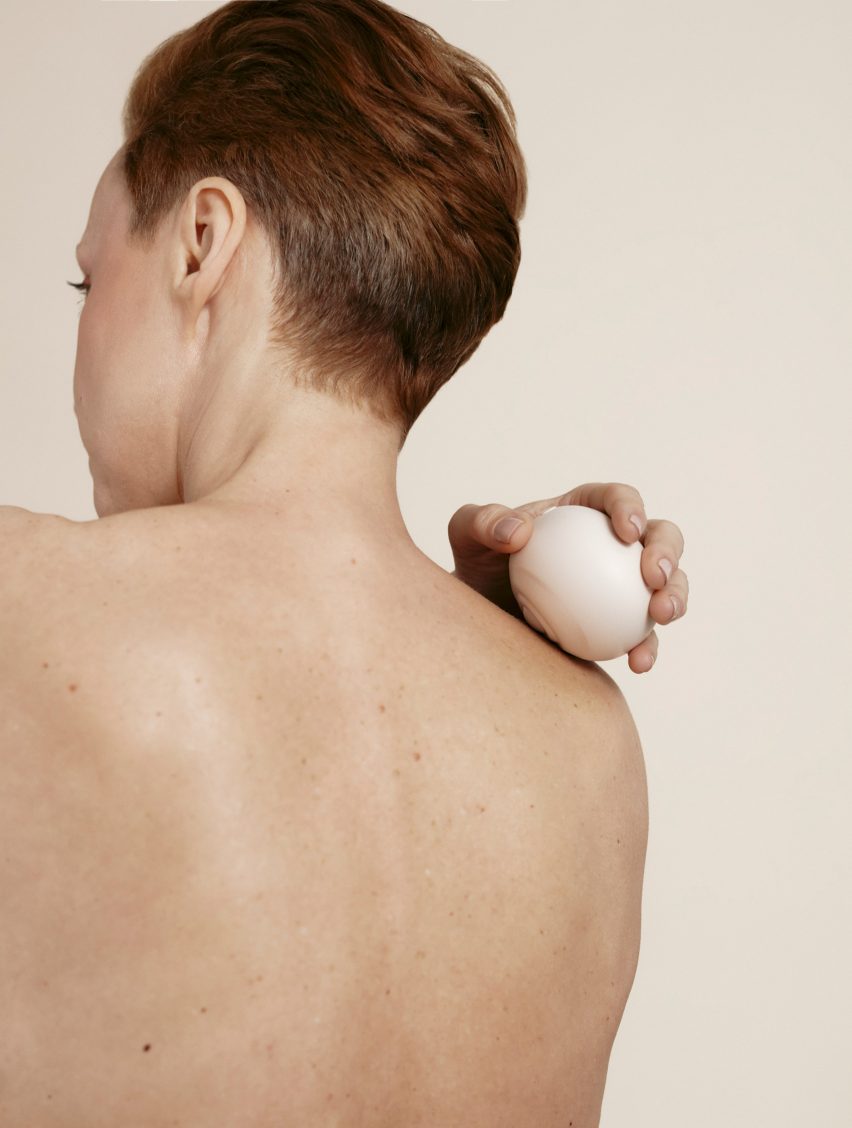 Photo of a woman's naked back as she holds the Tides massager to her right shoulder