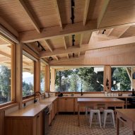 A kitchen in a timber structure with wooden units and large windows