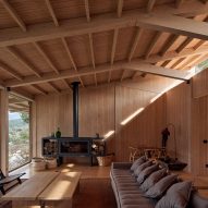 A living room in a timber structure with a pitched roof, decorated with a grey sofa, lounge chairs and a black fireplace