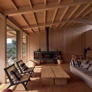 Open-plan living room with a grey sofa, black fireplace and lounge seats in a timber room