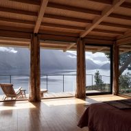 A bedroom in a timber structure with glass doors leading to an terrace overlooking a lake