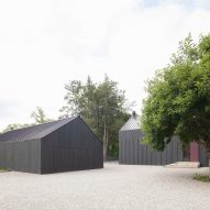 Black timber-clad structures on gravel ground