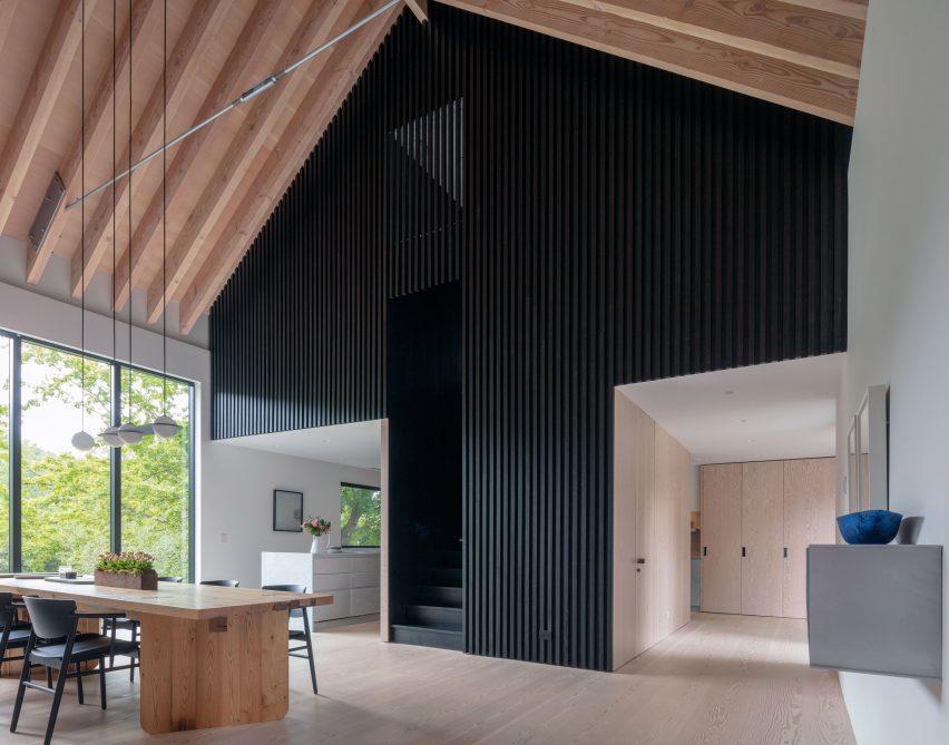 Espacio habitable de planta abierta con techo inclinado de madera a la vista y hastial con paneles de madera negra