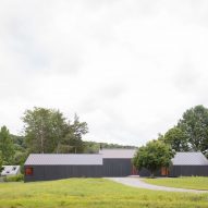 Three black timber barn-like buildings surrounded by trees