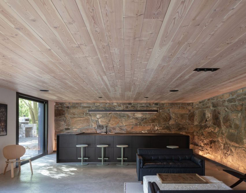 Sala de estar y bar en una casa con techo de madera y pared de piedra