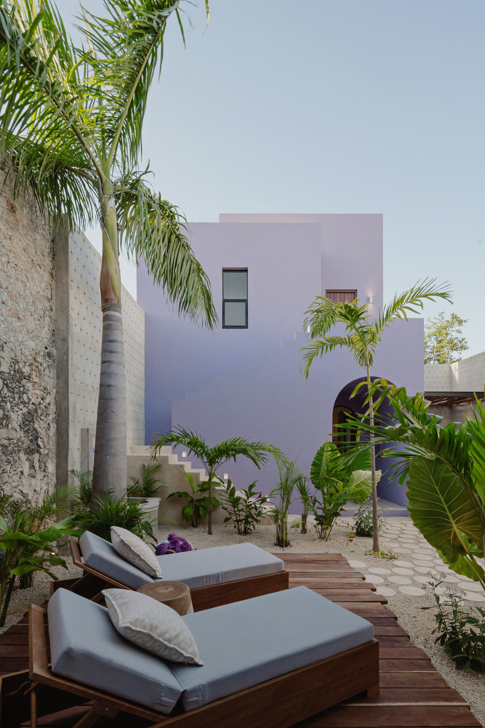 Purple two-storey cuboid house with sun lounges and palm trees