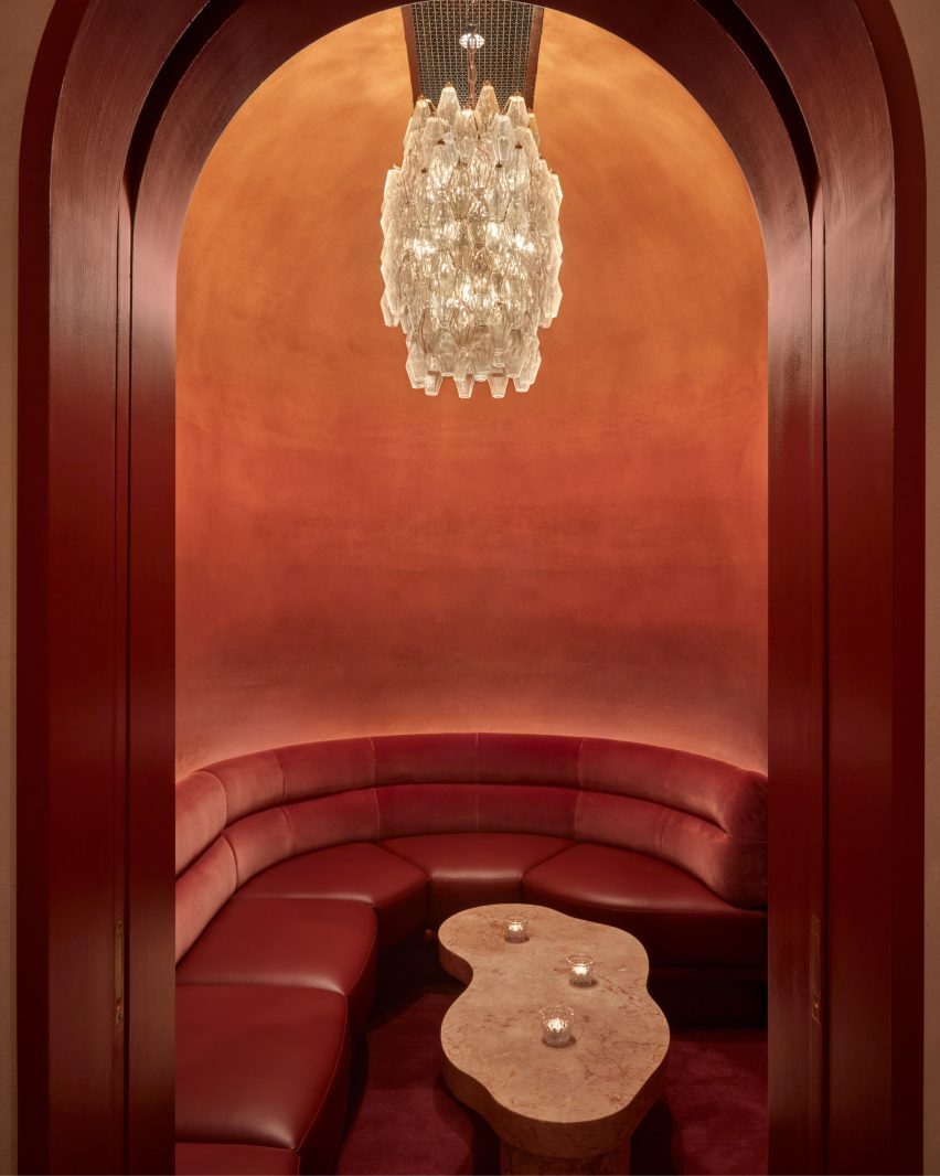 Curved burnt-orange alcove in a restaurant with red bench seating and a chandelier